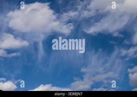 Bright blue sky filled with soft white clouds and delicate cirrus streaks forming abstract patterns. Clean natural background with gentle gradients, i Stock Photo