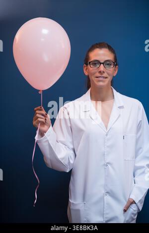 Female doctor in lab coat holding a pink balloon in a medical testing laboratory Stock Photo