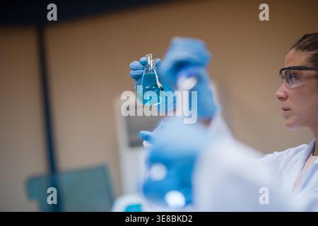Young medical technicians and doctors analyzing blue blood sample in clinical laboratory with PPE Stock Photo