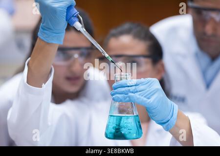 Young medical researchers performing pipette experiment in laboratory with gloves and safety goggles Stock Photo