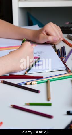 A close-up shot of a child drawing flowers in a sketchbook with various colored pencils on a white desk. Stock Photo