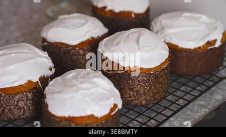Traditional gluten free Easter cakes (Kulich Easter breads) topped with white icing cooling on a wire rack. Stock Photo