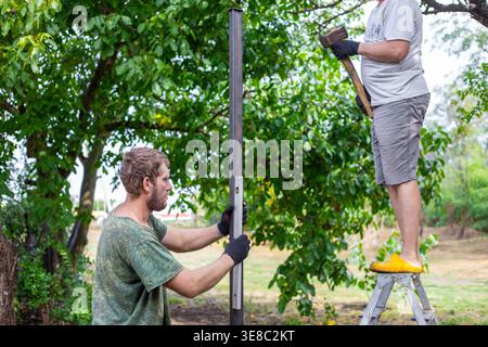 Builder using a spirit level on a metal post with a partner on a ladder nearby. Construction precision, professional work, home improvement. Stock Photo