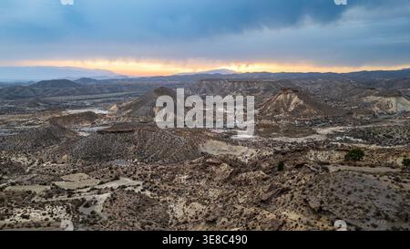 A spectacular aerial view captures the sun setting behind the mountains of the Tabernas Desert. Warm light illuminates the badlands' peaks and eroded Stock Photo