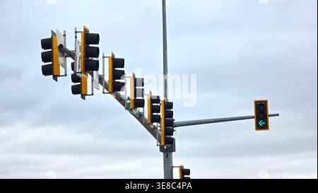 Traffic lights with green left turn arrow. Low angle view of multiple traffic signals at an intersection under a cloudy sky, featuring an illuminated Stock Photo