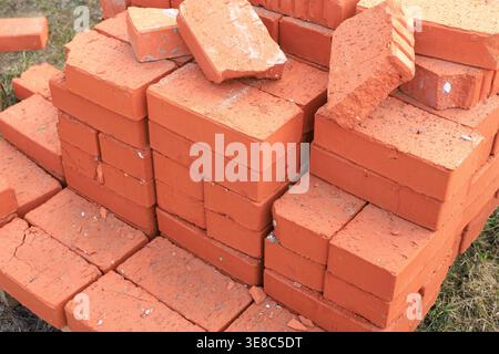 Large pile of red ceramic bricks stacked on a wooden pallet at a construction site. High-quality clay masonry units ready for building walls, home ren Stock Photo