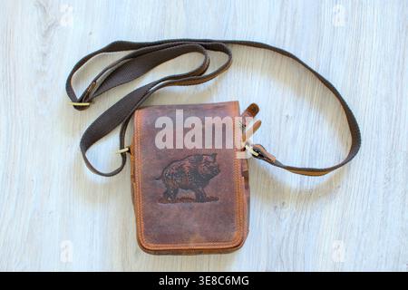 Overhead view of rustic brown leather messenger bag for men on grey wood grain flooring. Vintage style travel and outdoor accessory. Stock Photo