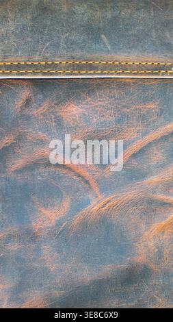 Macro texture of genuine distressed crazy horse leather with orange-gold horizontal stitching on top. Rustic brown cowhide background. Stock Photo
