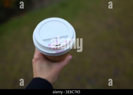 Hand holding takeaway coffee cup with lipstick mark, urban lifestyle detail and morning routine concept. Stock Photo