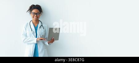 Doctor Using Laptop While Standing Against Plain Wall in Medical Setting Stock Photo