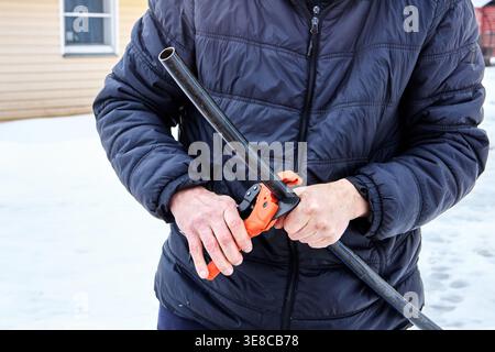 Ratchet pipe cutter in hands of plumber working with HDPE pipes. Stock Photo