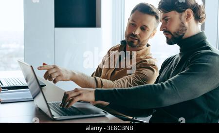 Two Men Discuss Ideas While Working on a Laptop in an Office Setting During the Day Stock Photo