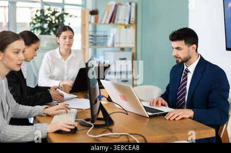 Young man works on laptop with colleagues Stock Photo