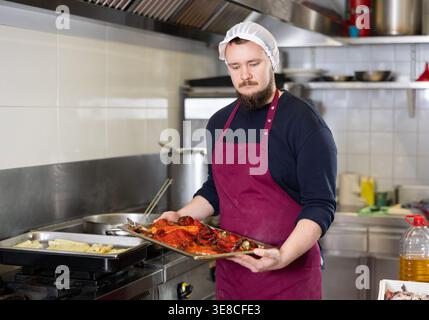 Bearded chef preparing vegetable dishes for sale in deli section of store Stock Photo