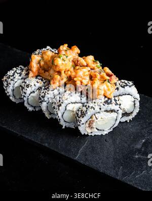 Sushi rolls topped with orange crab mixture. Black slate background emphasizes rich colors. Crunchy sesame seeds add texture and contrast. Sushi is ar Stock Photo
