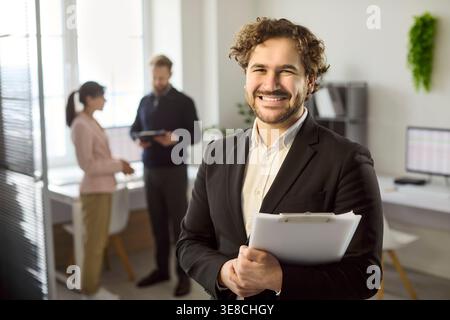 Smiling business manager portrait in office, confident employee with clipboard Stock Photo