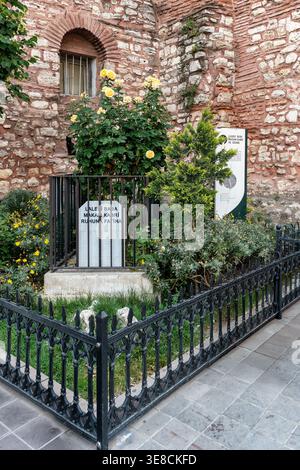 Istanbul, Turkey - June 05, 2025: Laleli Baba Tomb and Fountain with an ancient stone wall, barred window, and vibrant yellow roses in a garden setting Stock Photo
