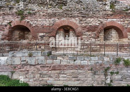 Weathered stone and brick wall with three arches, one featuring a small window, and a metal railing. Walls of Constantinople, Istanbul, Turkey Stock Photo