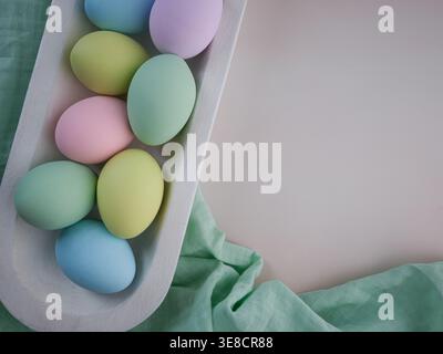 Overhead colorful pastel Easter eggs in white wood farmhouse rustic bowl tray on green muslin cloth. Spring decor card background Stock Photo