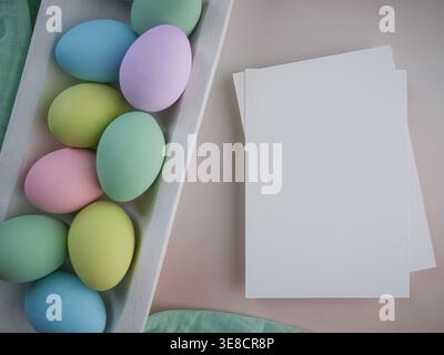 Blank empty card note paper overhead colorful pastel Easter eggs in white wood farmhouse rustic bowl tray on green muslin cloth. Spring decor card Stock Photo