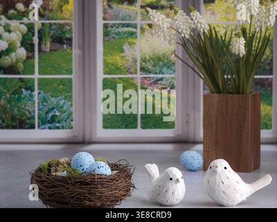 Bright kitchen with colorful peaceful nature garden window and Spring robin nest with blue speckled spotted eggs. Carved wood white birds. Brown wood Stock Photo