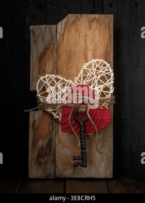White woven straw and red yarn hearts with rustic vintage key tied to farmhouse country wood plank. Dark and black wood table and moody background. Stock Photo