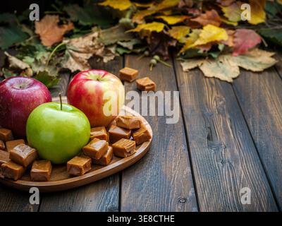 Fall wood plank table with apples and caramel on brown wooden plate with autumn leaves Stock Photo