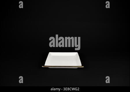 Empty white and gold ceramic square appetizer plate with gold rim on black background Stock Photo