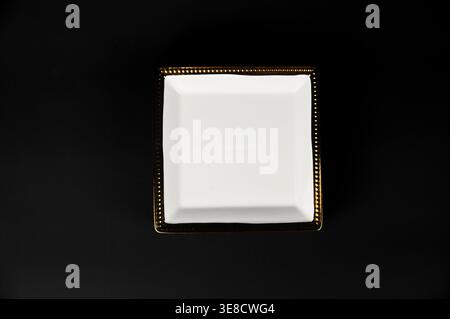 Empty white and gold ceramic square appetizer plate with gold rim on black background Stock Photo