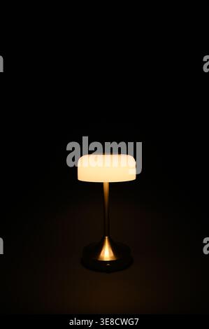Small white lamp shade on brass lamp post with glowing warm light Stock Photo