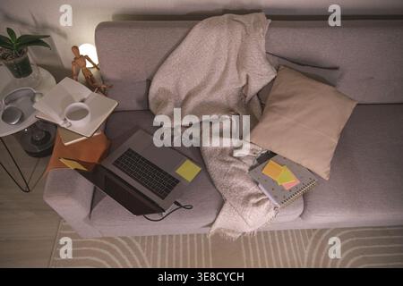 Sofa offering a comfortable space for remote work and digital education with a laptop, books, and coffee Stock Photo