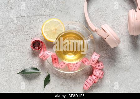 Cup of diet tea with lemon slice, measuring tape and headphones on grunge background. Weight loss concept Stock Photo