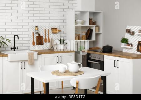 Stylish light kitchen with pegboards and modern dining table Stock Photo
