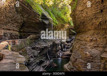 Stone walkway and small waterfalls inside narrow gorge at Watkins Glen State Park in New York with layered rock cliffs and filtered sunlight Stock Photo