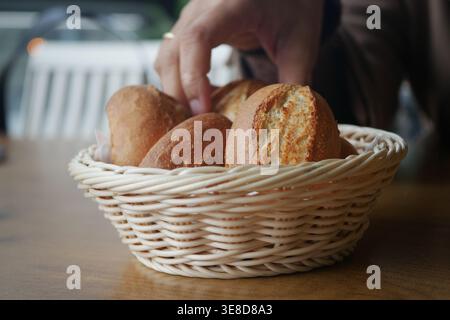 Hand reaches for bread in a basket on a table Stock Photo