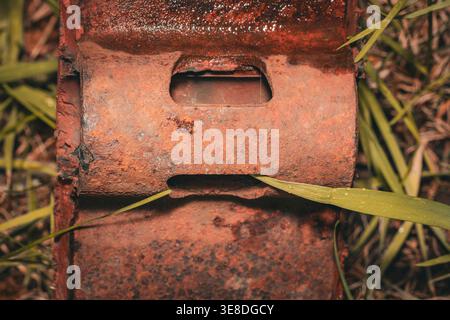 Top down view of a heavy rusted iron plate with rectangular holes laying in green grass, showing deep orange corrosion and weathered metal texture Stock Photo