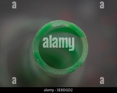 Top down macro close up view looking down the open end of a hollow green plastic drinking straw with a blurred grey background Stock Photo