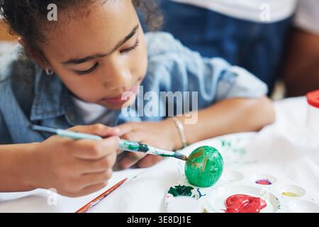 Girl, paintbrush and easter eggs with smile in house for festival, learning or love with parents. Child, decoration and color with painting, art and Stock Photo