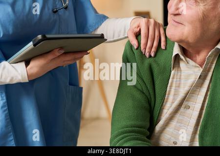 Senior Caucasian man receiving support from female nurse holding tablet during home care visit. Useful for healthcare services, elder care, patient communication marketing Stock Photo