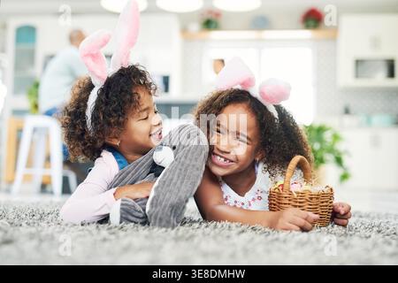 Easter eggs, basket and children in home for celebration, family and siblings with treats for event. Creative, snacks and girls with colorful sweets Stock Photo