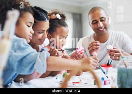Painting, parents and children with easter eggs in home, color or decoration for festive celebration. Happy, people and bonding with kids on Christian Stock Photo
