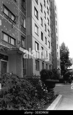 Slavyansk, 1980s. An architectural view of the entrance to a modern multi-story tiled residential building, featuring a geometric concrete canopy over the doorway and massive decorative flower urns placed along the walkway. This authentic vintage black and white photograph captures the aesthetics of late Soviet urban housing developments, highlighting the standardized yet uniquely decorated living environments of the era. A nostalgic glimpse into a peaceful Donbas before the war. Stock Photo