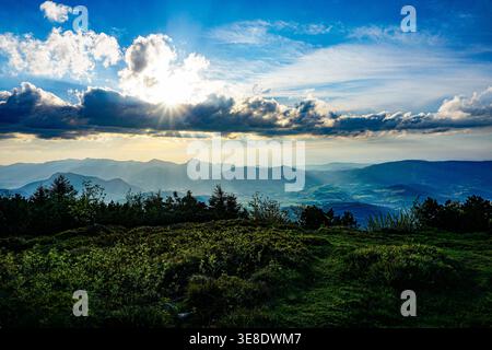 Sunset view of a mountainous landscape with rays of sunlight streaming through the clouds. Stock Photo