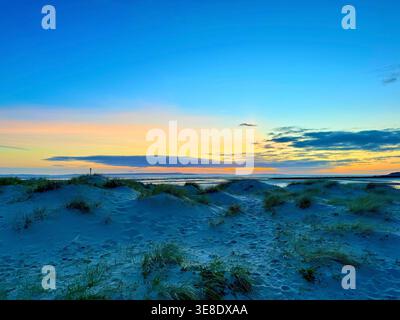 The blue hour, or sweet light moment, before sunset characterised by Rayleigh scattering making the sand dunes appear blue. Twilight beach scene Stock Photo