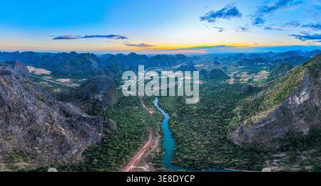 Towering mountain cliffs stand proudly beneath a clear blue sky, while fluffy white clouds float gently overhead, highlighting the beauty and serenity Stock Photo