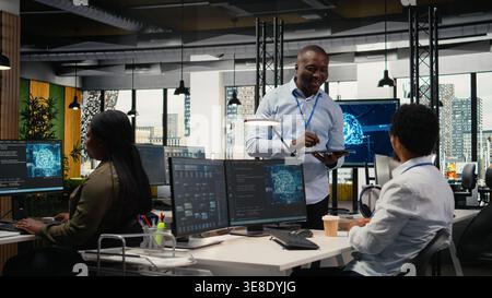 Smiling IT staff members in office using AI to optimize company systems performance. Happy colleagues in startup office use artificial intelligence technology to automate tasks, camera A Stock Photo