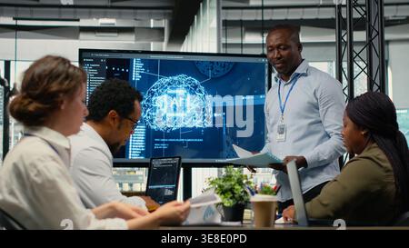 Programmer gives presentation to executives, implementing AI chatbot reducing work volume. Startup office IT expert analyzing business insights for management using artificial intelligence, camera B Stock Photo