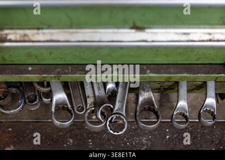 Various metal wrenches hanging from a magnetic strip inside a worn green tool cabinet, representing concepts of repair, maintenance, and industrial wo Stock Photo