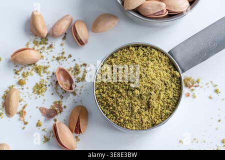 Ground pistachios in measuring cup with pistachio nuts on light background Stock Photo