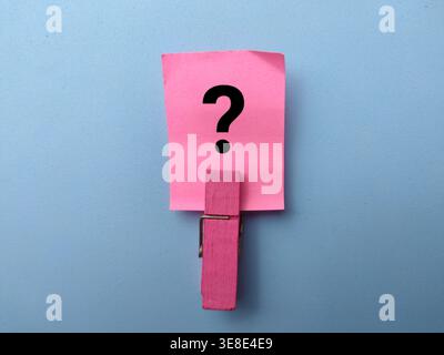 Pink paper note with a large black question mark, held vertically by a pink wooden clothespin. Stock Photo